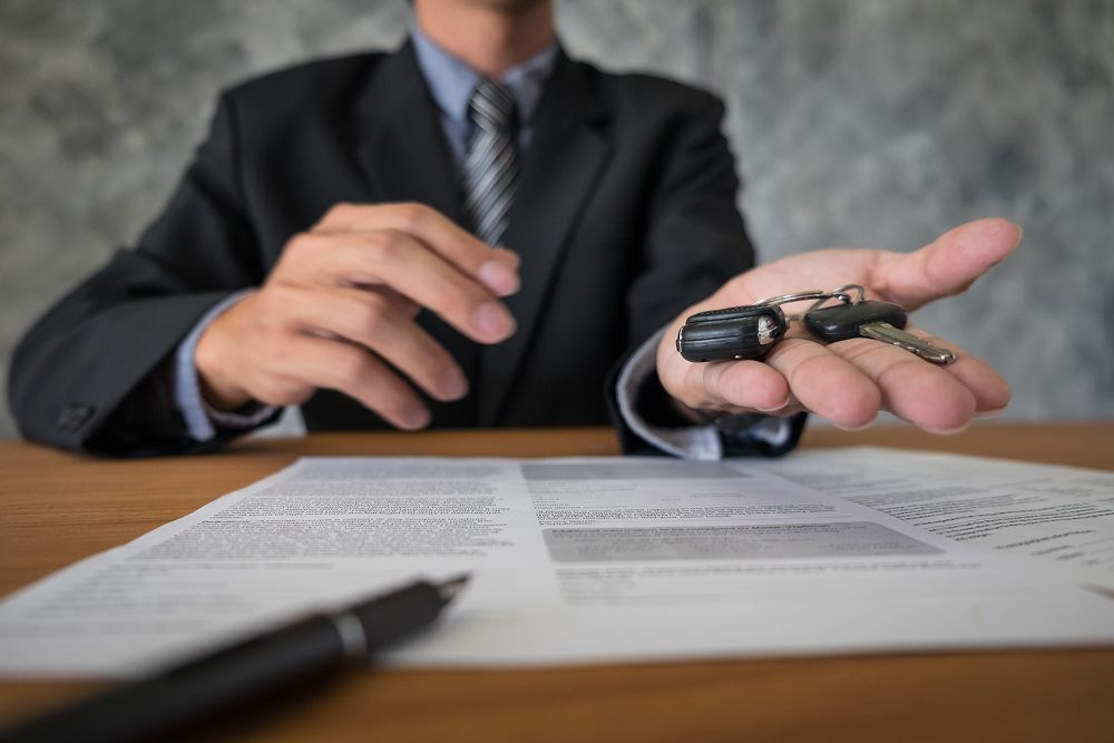 Bărbat care întinde cheile unei mașini împreună cu contractul de închiriere auto
